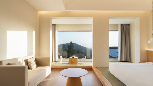 A hotel room with a bed, a sofa, a round table, and a view of a mountain and water. - Leisure Haven - Tachuan Hotel (Huangshan)