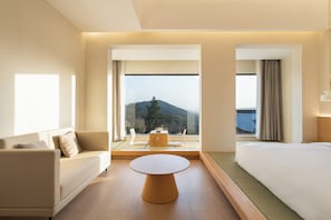 A hotel room with a bed, a sofa, a round table, and a view of a mountain and water. - Leisure Haven - Tachuan Hotel (Huangshan)