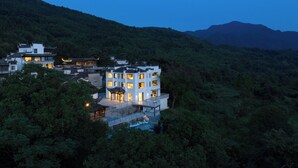 A multi-story building with traditional architecture, surrounded by lush greenery and mountains in the background. - Leisure Haven - Tachuan Hotel (Huangshan)