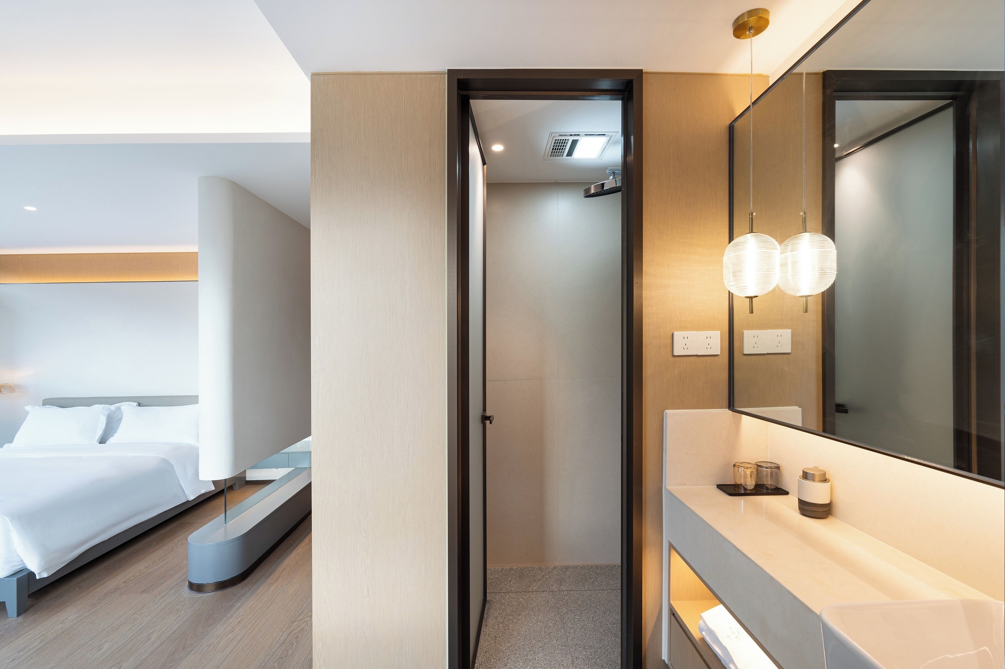 A modern hotel room with a bed, a bathroom with a mirror, and a vanity with a sink.