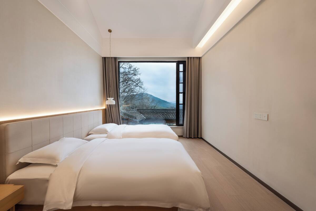 A hotel room with a large bed, a bedside table, a nightstand, and a view of a mountain through a window.
