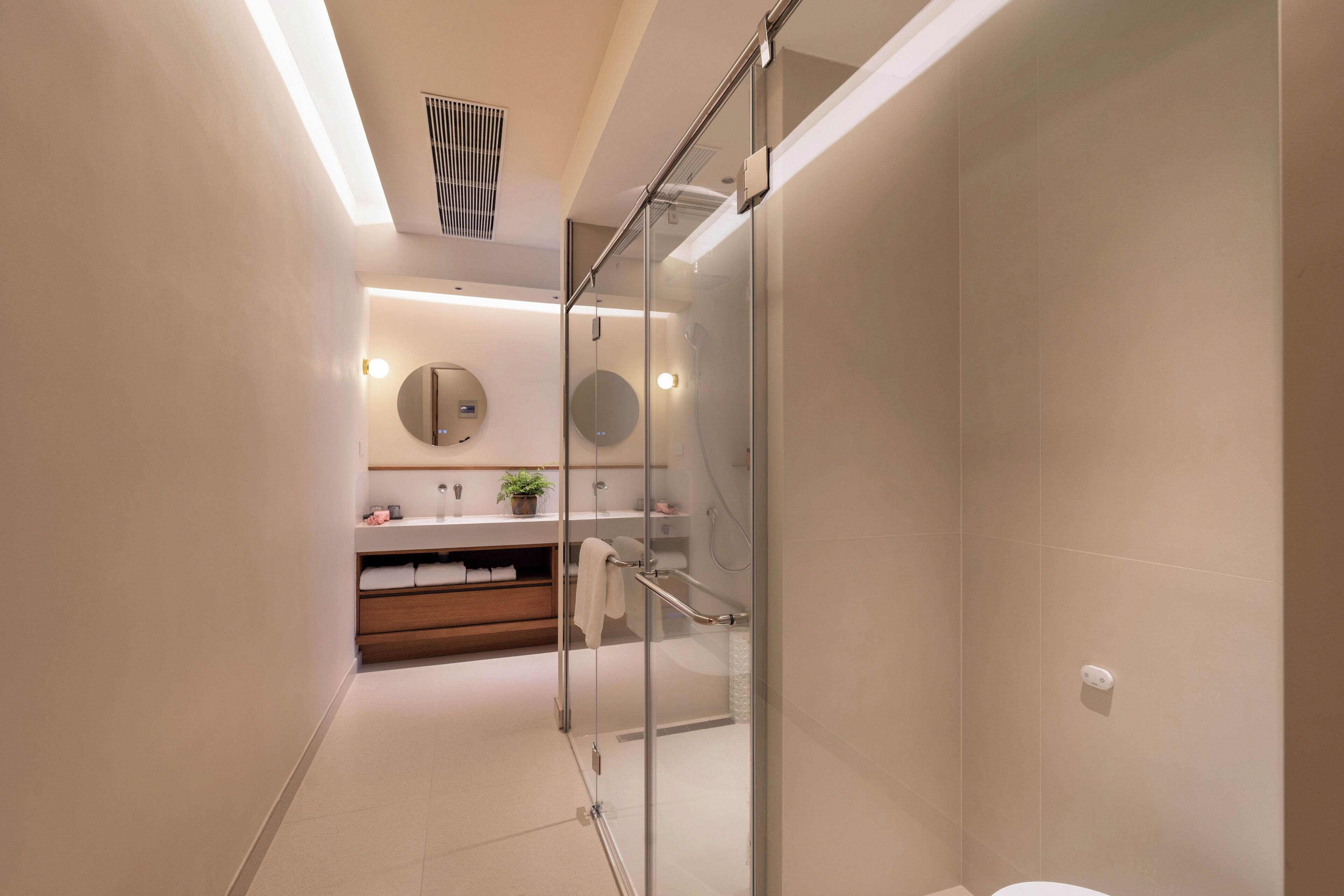 A modern bathroom with a glass shower enclosure, a wooden vanity, and a round mirror.