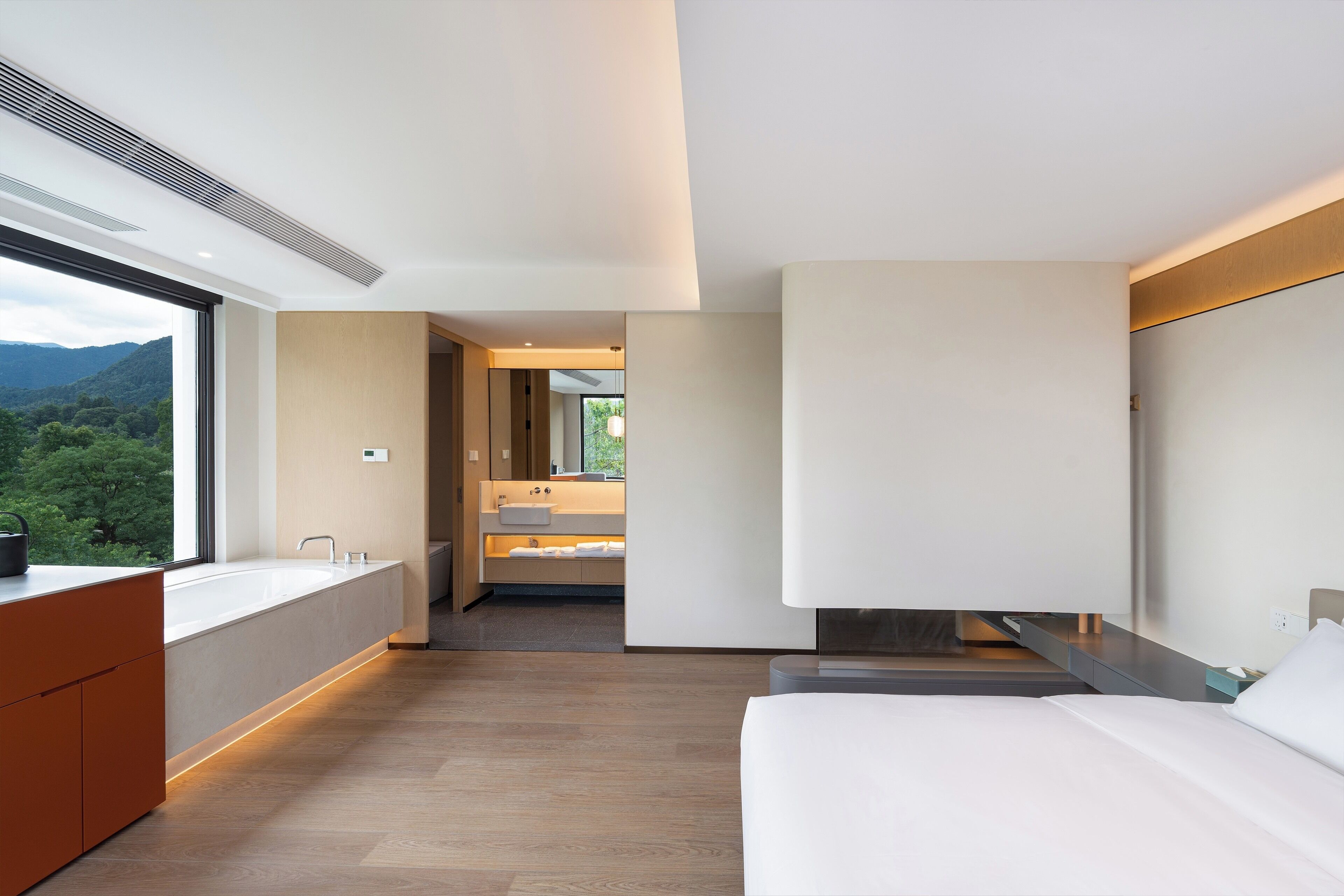 A modern hotel room with a large window, a built-in sink, a bed, and a walk-in closet.