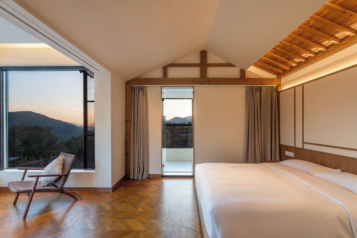 A bedroom with a large window, a wooden ceiling, and a bed.