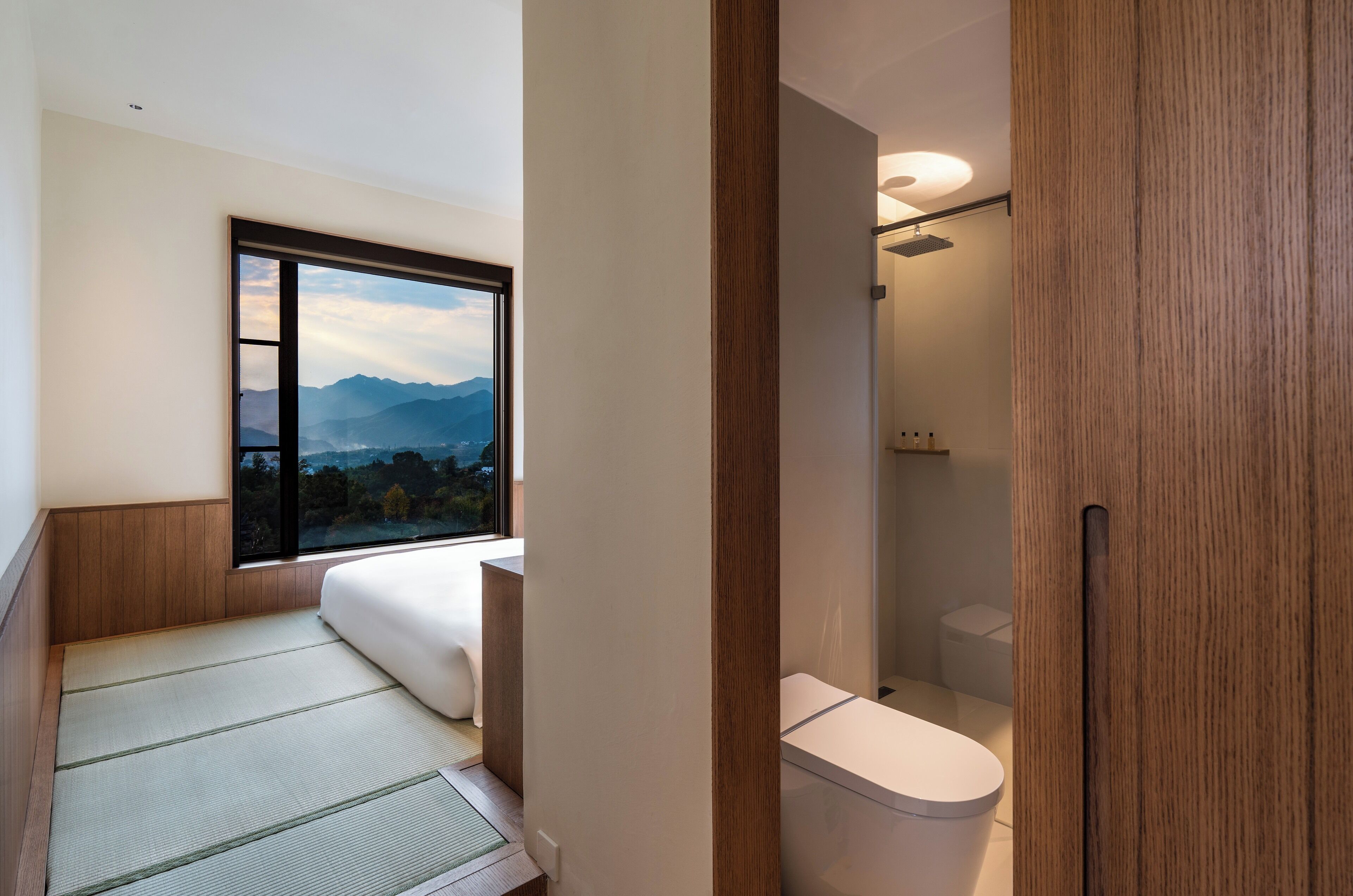 A modern bathroom with a toilet, a shower, and a window offering a mountain view.
