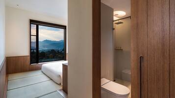 A modern bathroom with a toilet, a shower, and a window offering a mountain view.