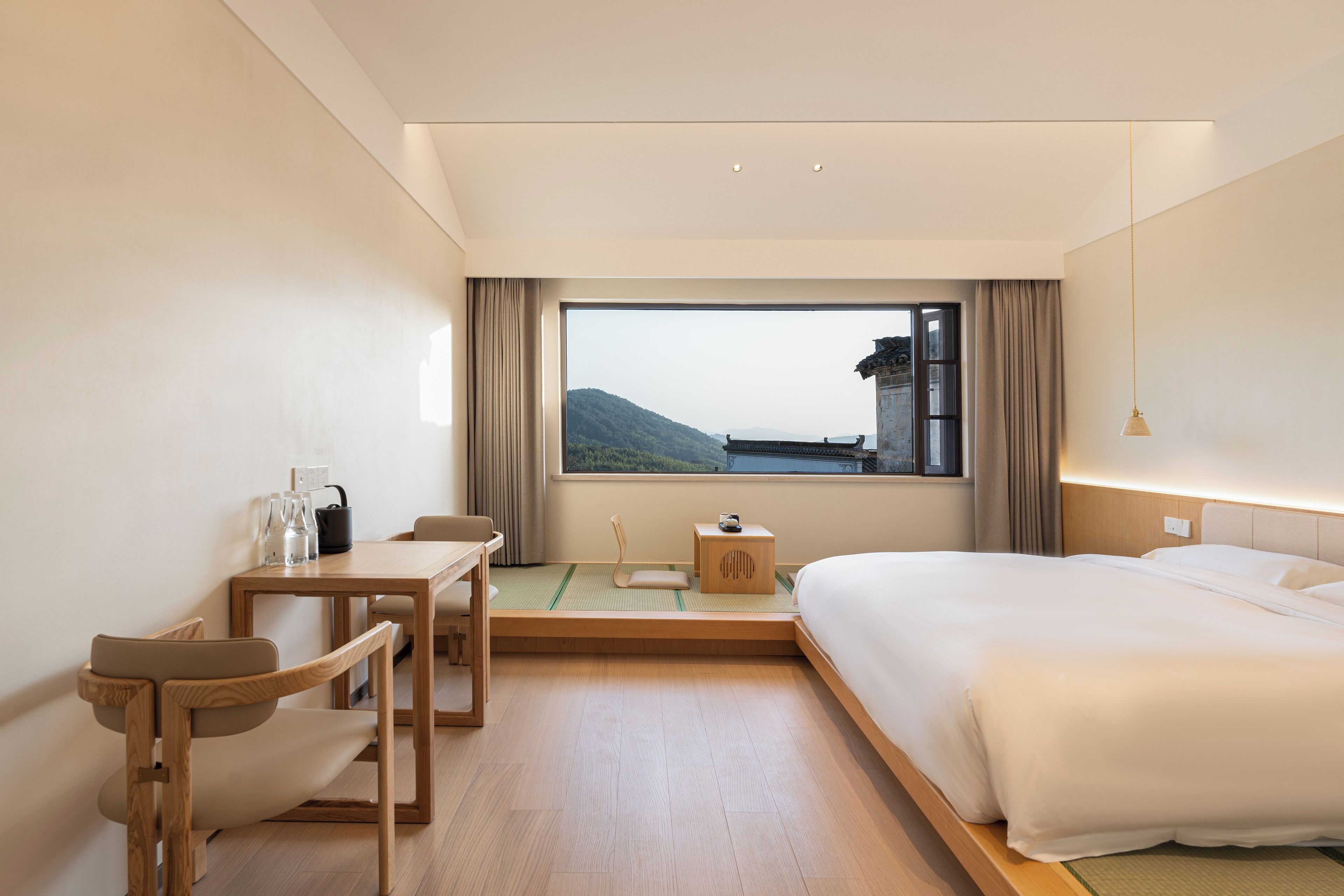 A modern hotel room with a large bed, a desk, and a view of a mountain through the window.