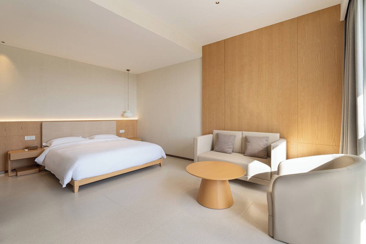 A modern hotel room with a bed, a sofa, a coffee table, and a wooden accent wall.