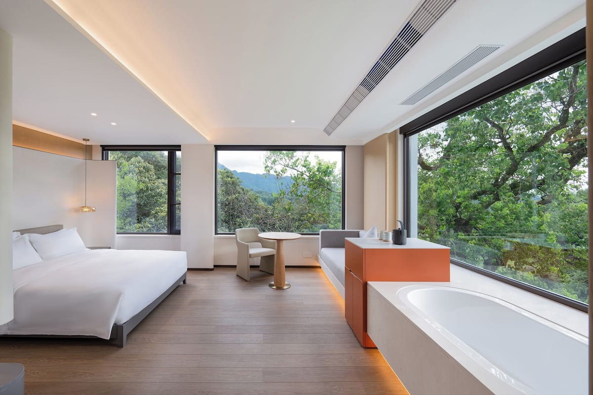 A modern bedroom with a large bed, a small table, a sofa, and a bathtub.