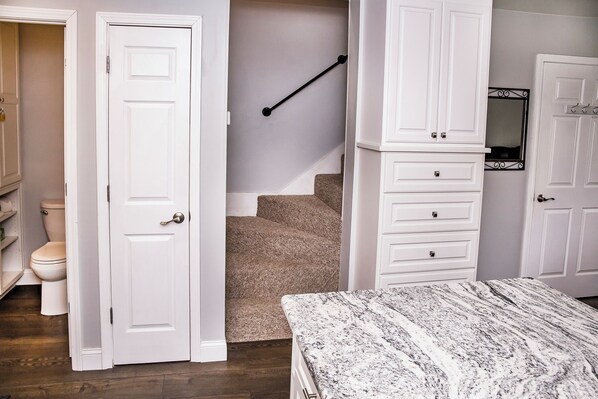 A bedroom with a bed, a white wardrobe, a bathroom with a toilet, and a staircase.