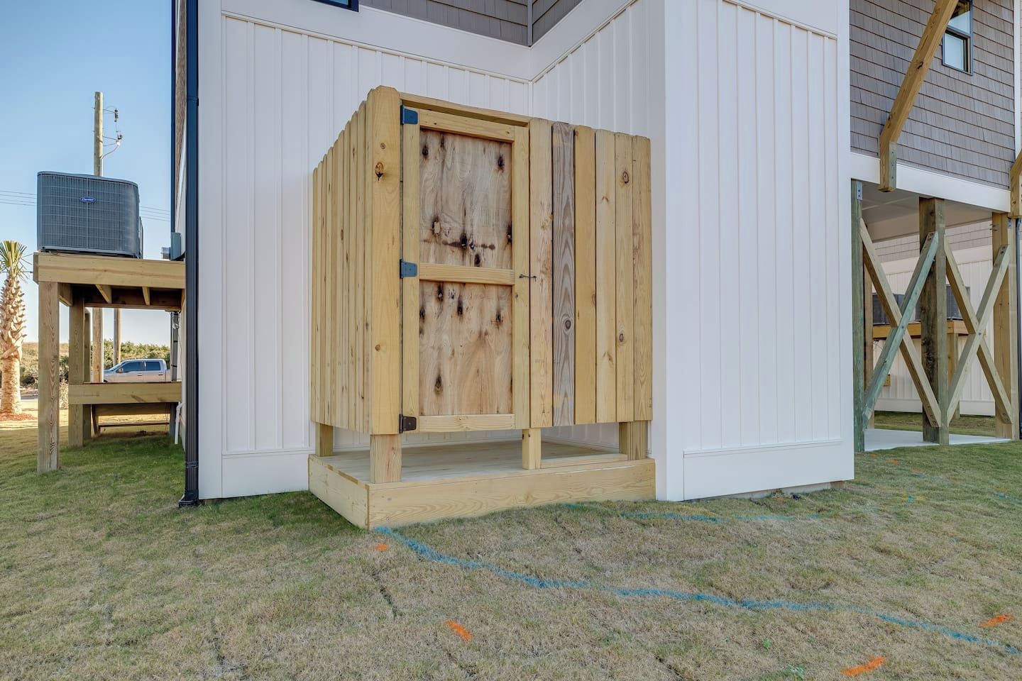 A wooden structure with a door, possibly a shed or storage unit, adjacent to a building with white siding.