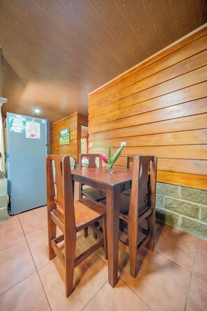 A wooden dining table with chairs, a refrigerator, and a wall with wooden paneling.