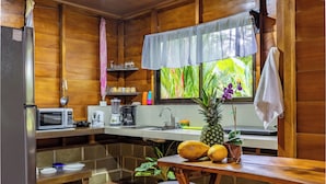 Cocina compacta con paredes de madera, microondas, pileta y ventana con vista a vegetación.