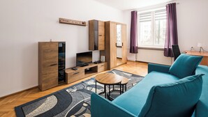Una sala de estar moderna con un sofá, un televisor, un mueble de madera y un ventanal con cortinas.