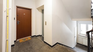 Un pasillo con una puerta de madera marcada con el número 50, un felpudo, una pared blanca y una ventana que muestra un coche estacionado.