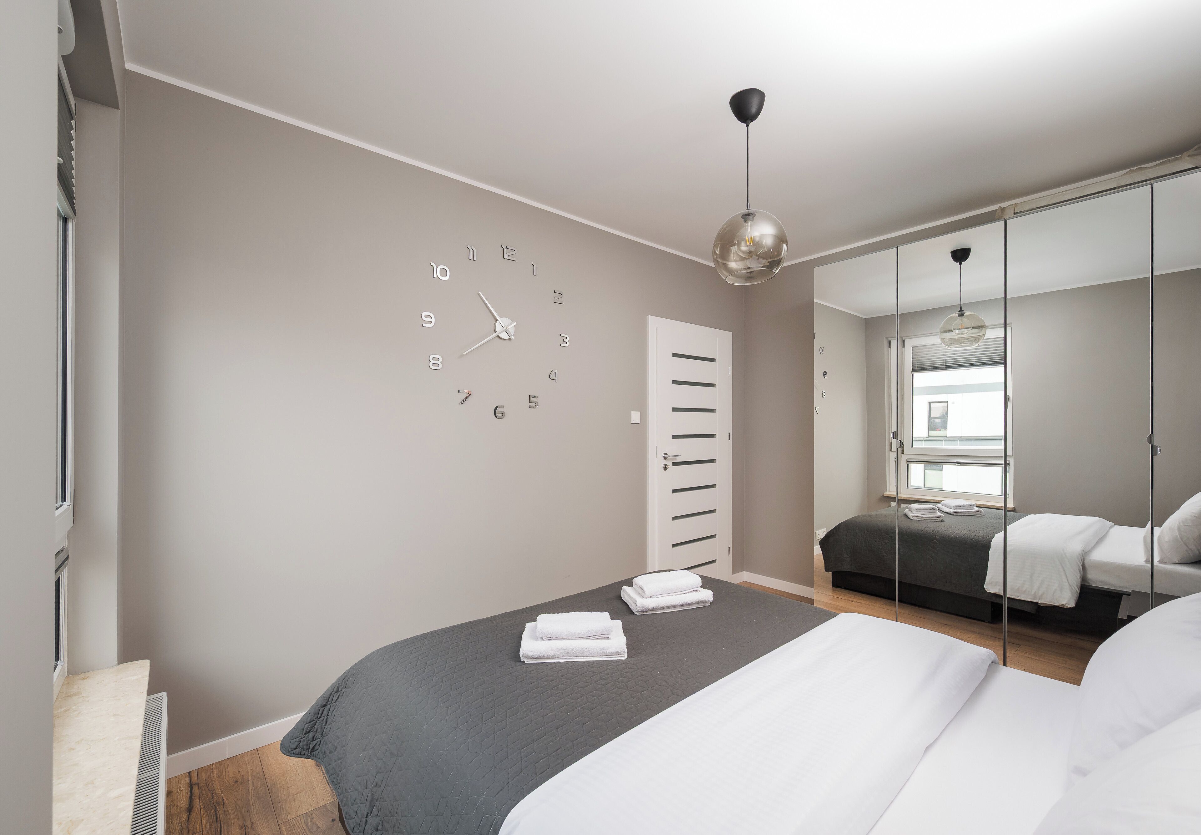 A modern bedroom with a large bed, a wall clock, a wardrobe, and a hanging light fixture.