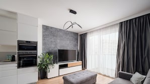 A modern kitchen with built-in appliances, a grey sofa, and a large window with curtains. - Raków Stylish Apartment (Warszawa)