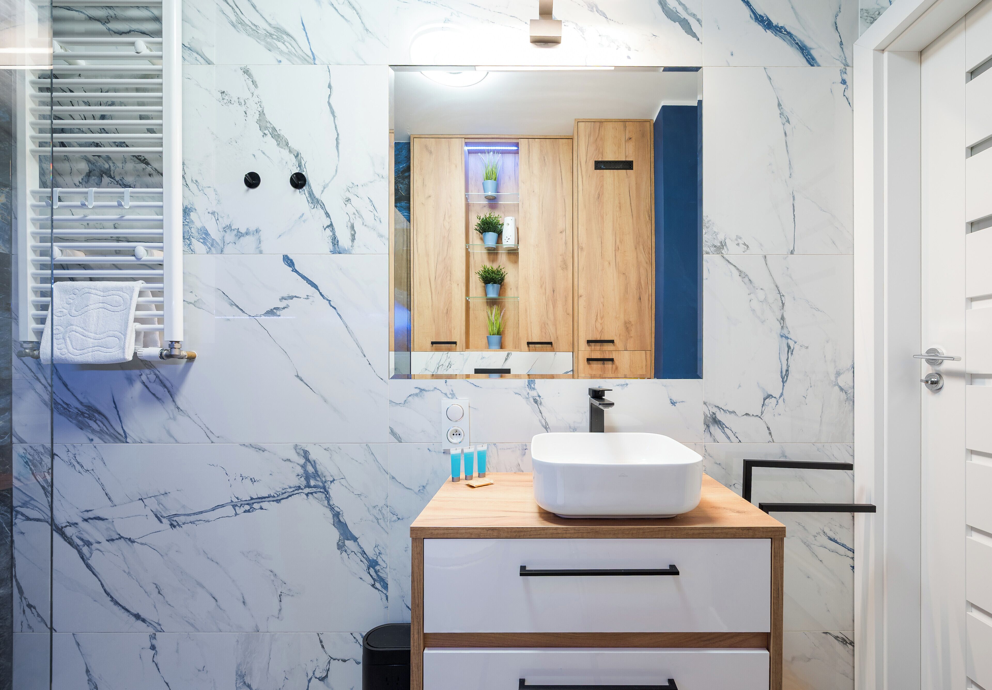 Une salle de bain moderne avec un pare-baignoire en marbre, un meuble-lavabo en bois, un lavabo blanc et un miroir.
