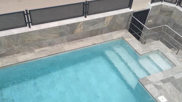 Ein rechteckiger Swimmingpool mit klarem, blauem Wasser, umgeben von Steinplatten und Metallgeländern.