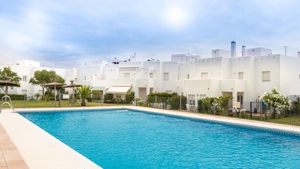 Una piscina con solárium empedrado, rodeada de edificios blancos con numerosas ventanas y balcones.