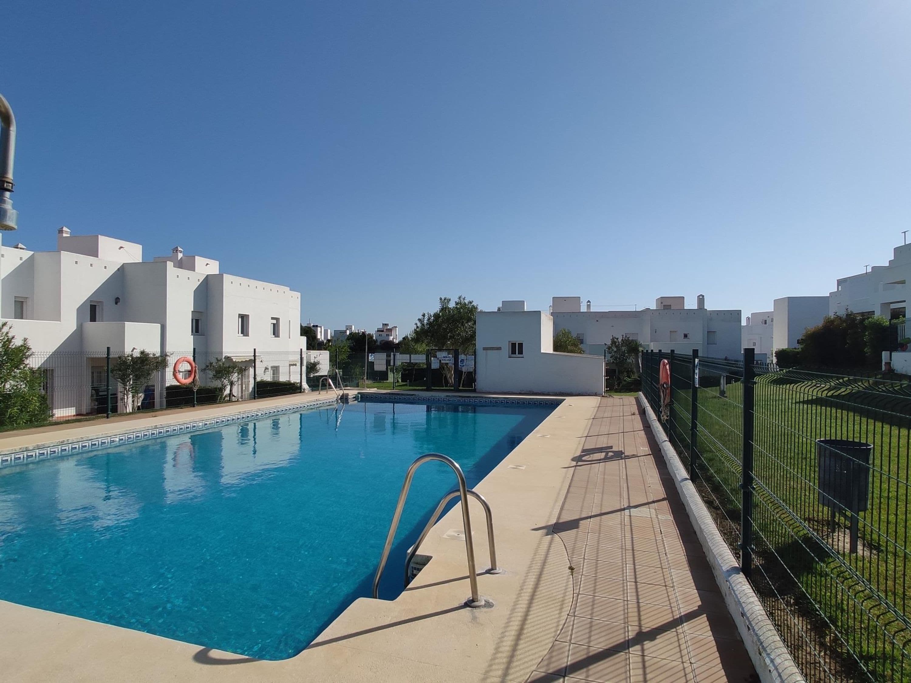 Ein Swimmingpool mit gefliestem Deck, umgeben von weißen Gebäuden mit Balkonen.