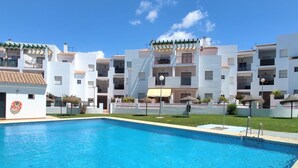 A swimming pool with a clear blue water surface, surrounded by white buildings with balconies and a covered outdoor seating area. - Rotonda VII 54 in Conil de la Frontera (Conil de la Frontera)