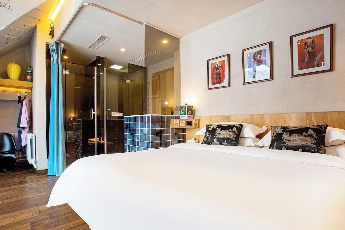 A hotel room with a large bed, a glass shower enclosure, and a wooden floor.