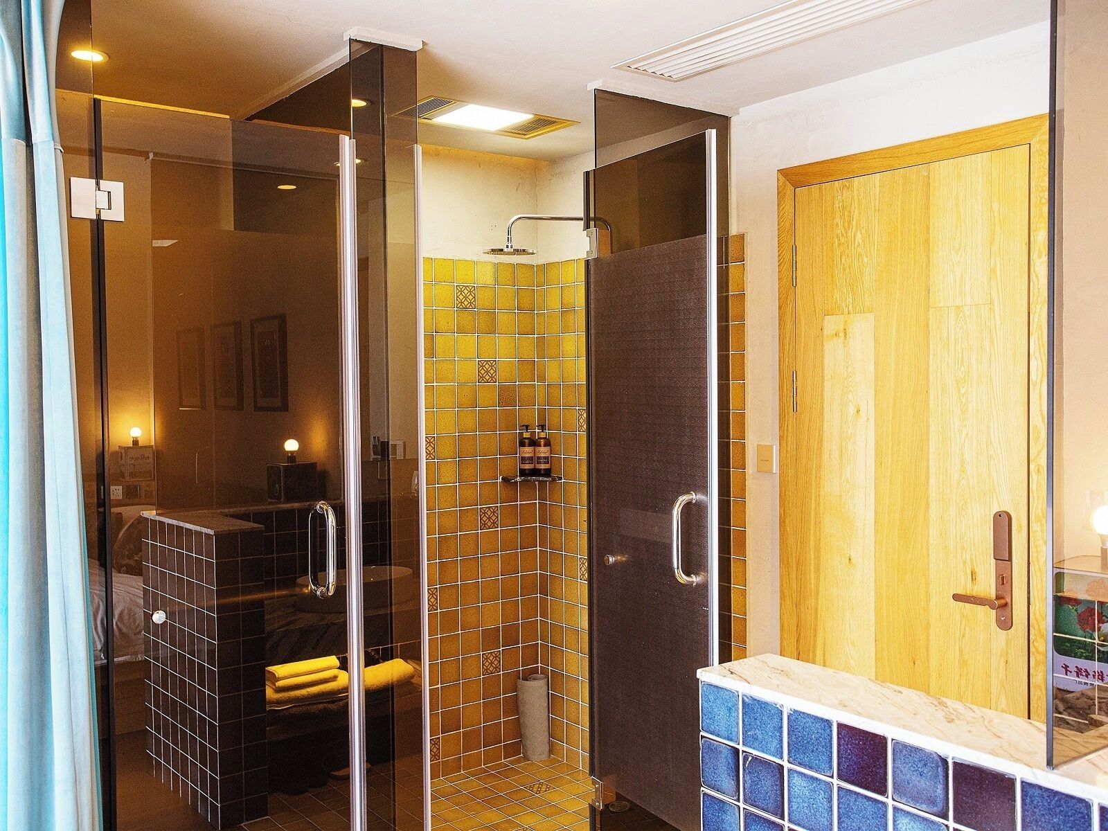 Un baño moderno con cabina de ducha de vidrio, puerta de madera y zona de lavabo con azulejos.