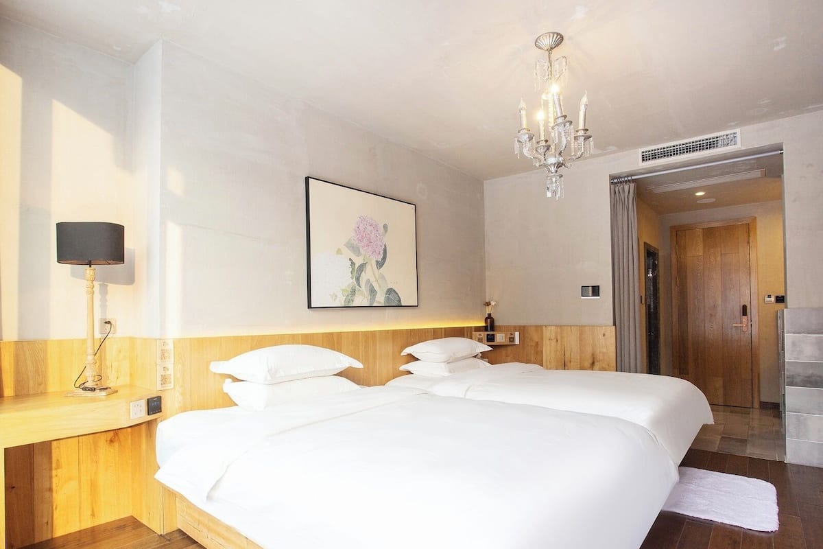 A hotel room with a large bed, a bedside lamp, a chandelier, and a painting on the wall.