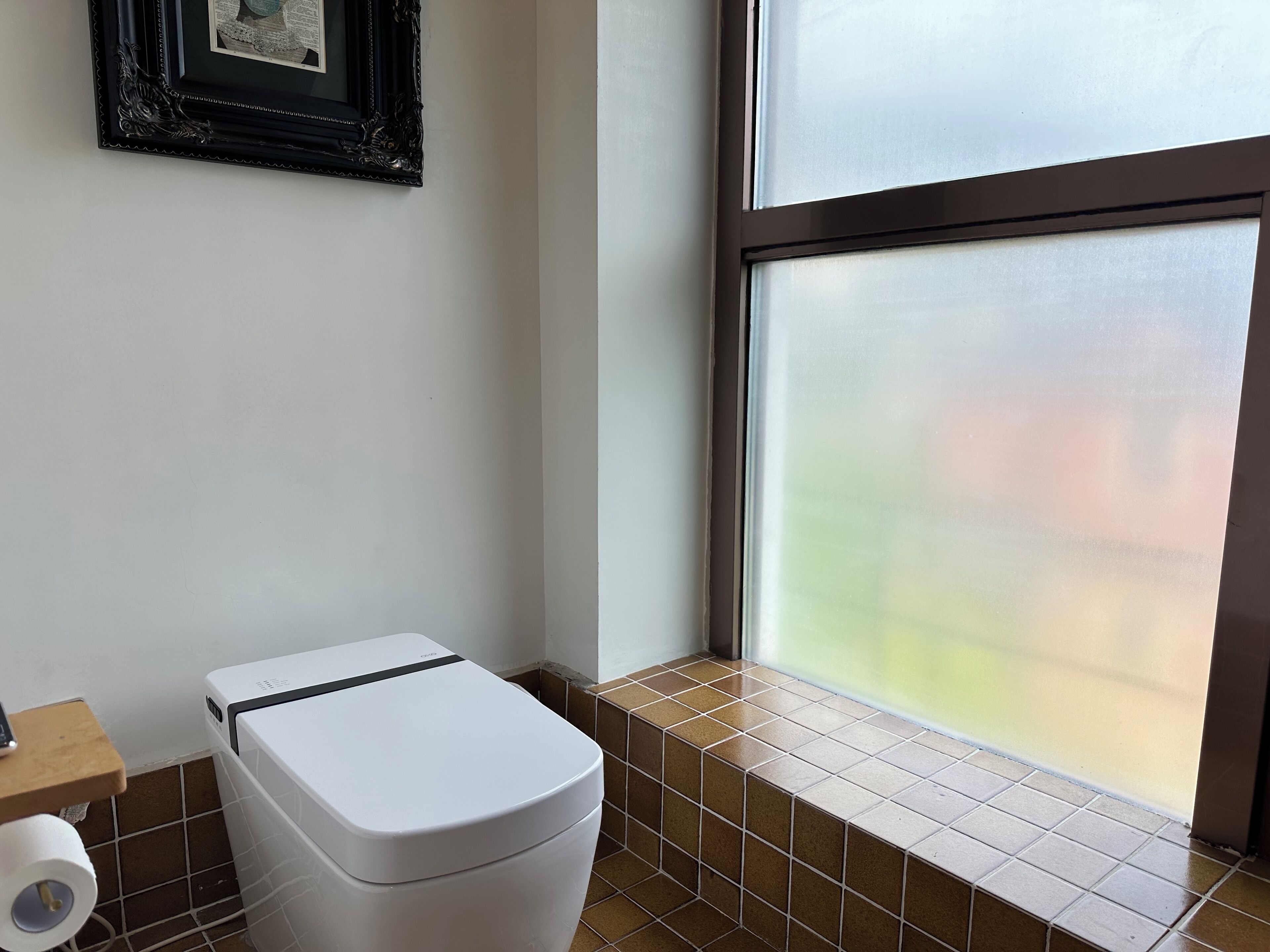 Un baño con inodoro blanco, un cuadro en la pared y un ventanal con vidrio esmerilado.