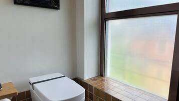 Un baño con inodoro blanco, un cuadro en la pared y un ventanal con vidrio esmerilado.