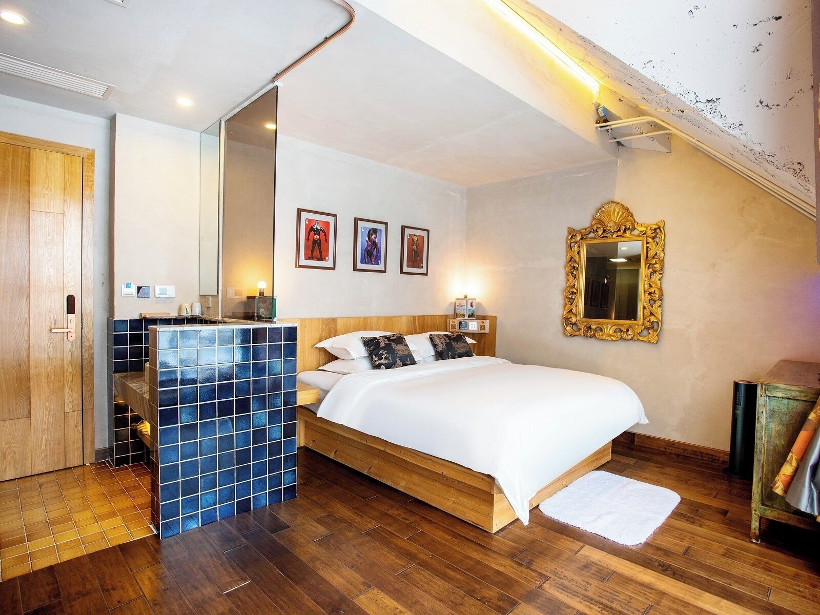 A bedroom with a wooden bed, a blue-tiled sink, a mirror, and framed pictures on the wall.