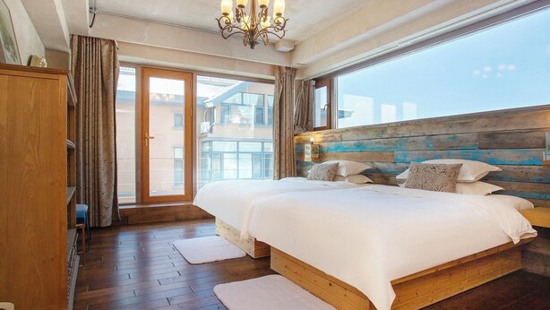 Une chambre à coucher avec une tête de lit en bois, un grand lit avec une literie blanche, un lustre et une vue sur l’extérieur.