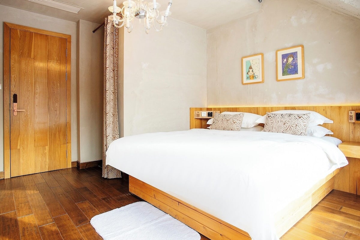 A bedroom with a large bed, wooden headboard, a chandelier, and two framed pictures on the wall.
