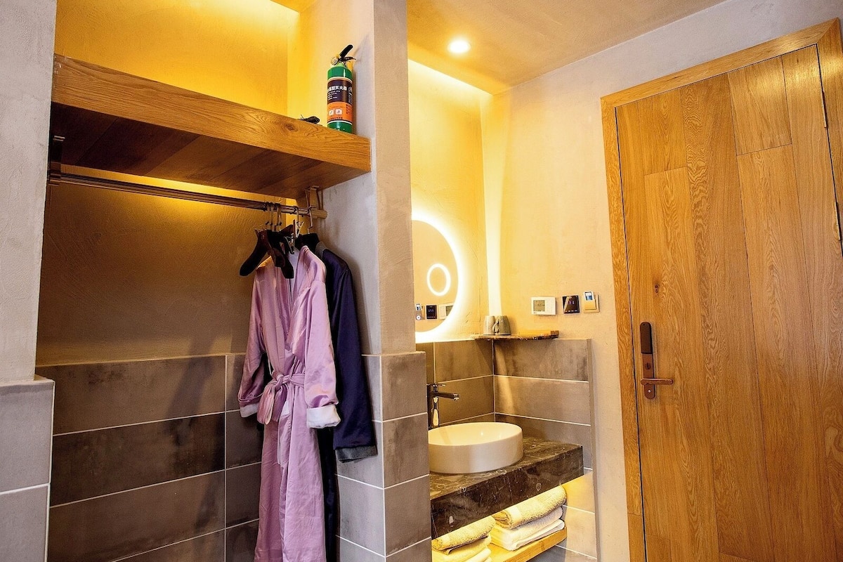 A modern bathroom with a wooden door, a sink, and a robe rack with two robes.