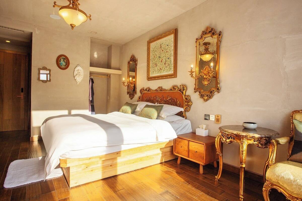 A bedroom with a large bed, a wooden nightstand, a small round table, and a chair.