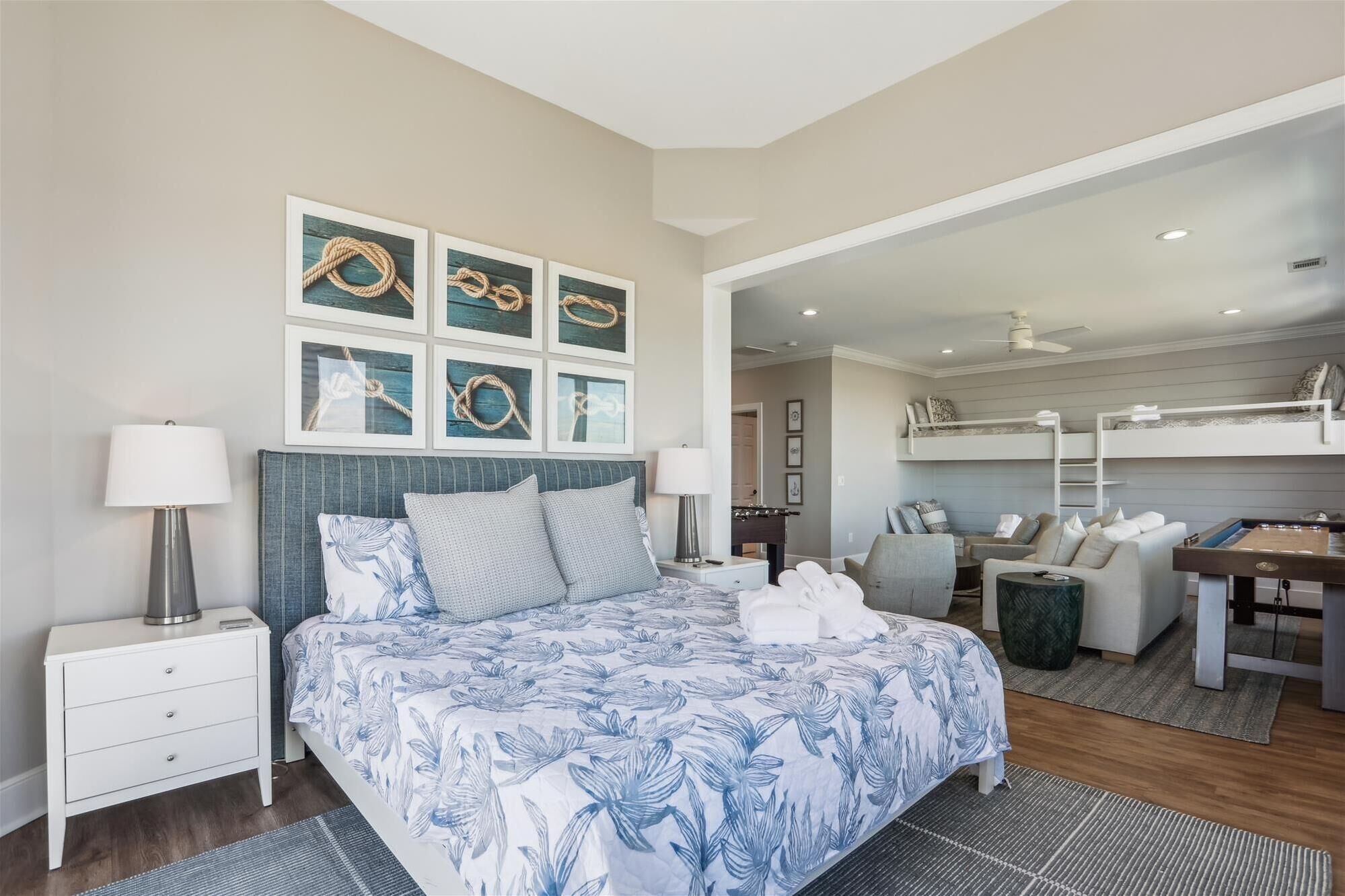 A modern hotel room with a large bed, a desk, and a bunk bed in the background.