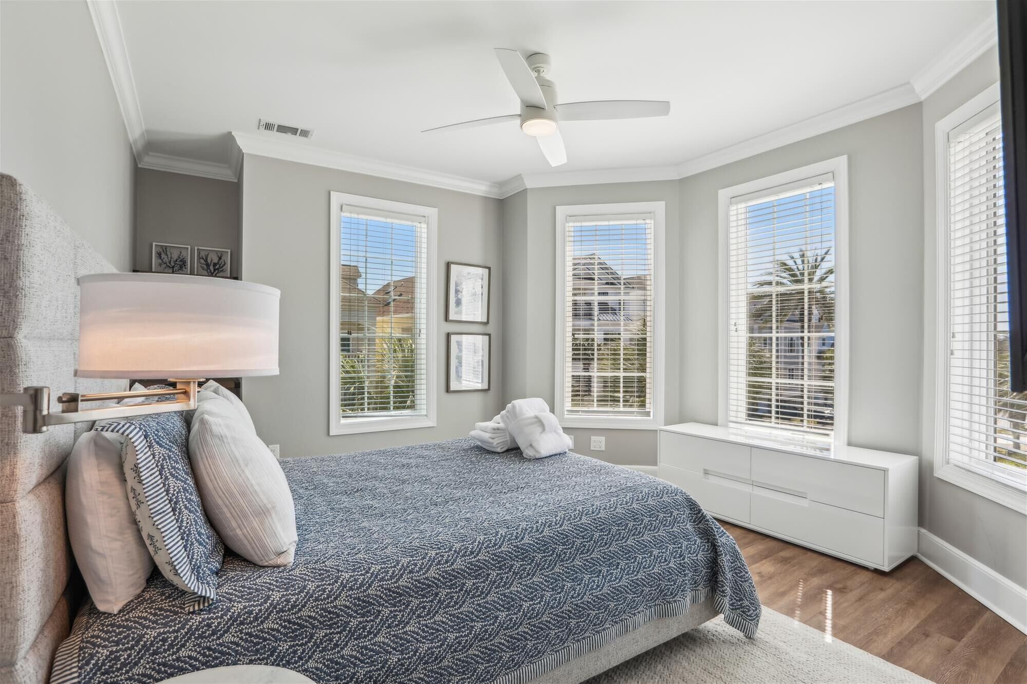 Un dormitorio con cama, ventilador de techo y ventanas amplias con persianas.
