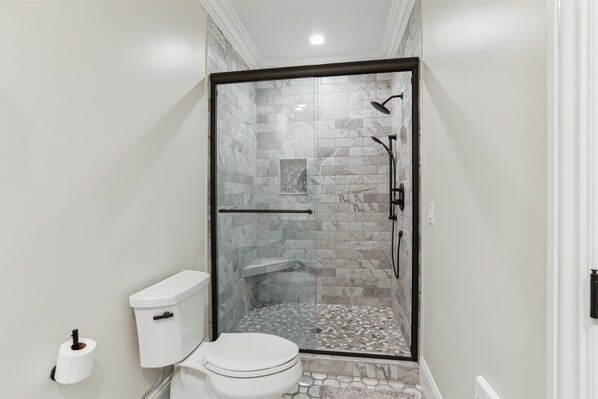 A modern bathroom with a glass-enclosed shower, a toilet, and a hand dryer.
