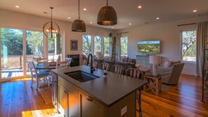 A spacious kitchen with a central island, large windows offering views of the outdoors, and a dining area with a TV mounted on the wall. - Unforgettable marsh views 4 bedroom home (North Charleston)
