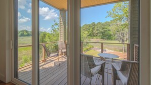 A covered outdoor area with a wooden deck, wicker furniture, and a view of a green landscape. - Unforgettable marsh views 4 bedroom home (North Charleston)
