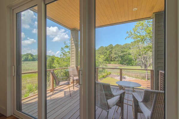 A covered outdoor area with a wooden deck, wicker furniture, and a view of a green landscape. - Marsh View 4Br Park Circle Home, Close to Downtown (North Charleston)