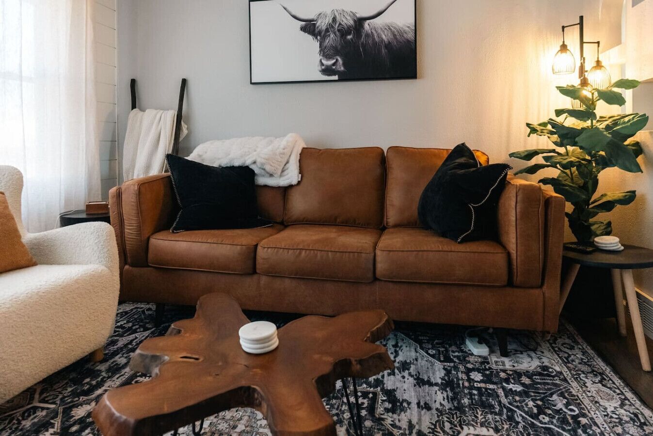 A brown leather sofa with black and white throw pillows, a wooden coffee table, a patterned rug, and a framed picture of a bull on the wall.