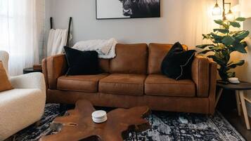 A brown leather sofa with black and white throw pillows, a wooden coffee table, a patterned rug, and a framed picture of a bull on the wall.