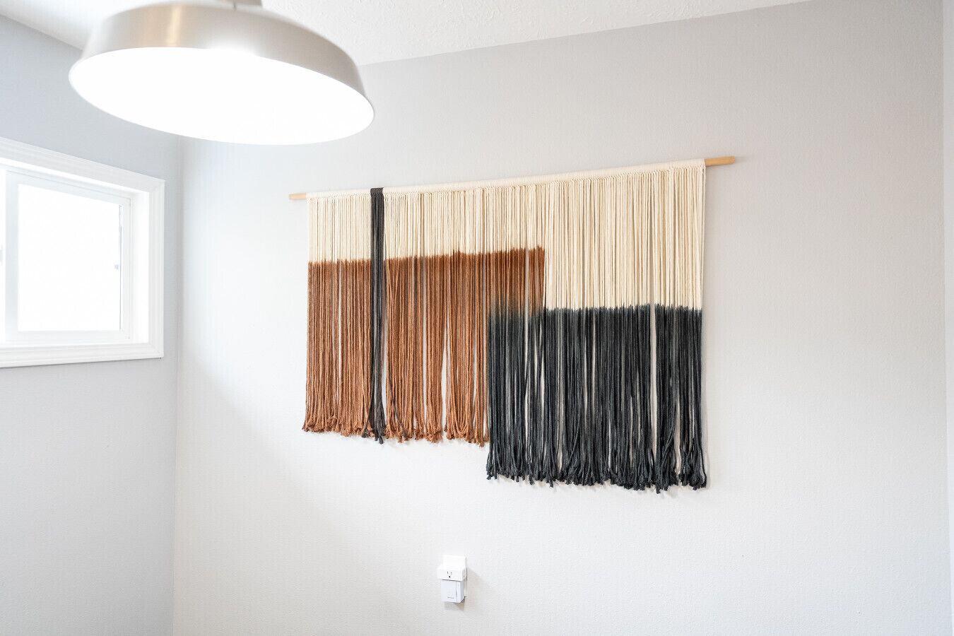 A wall with a macrame piece and a light fixture.