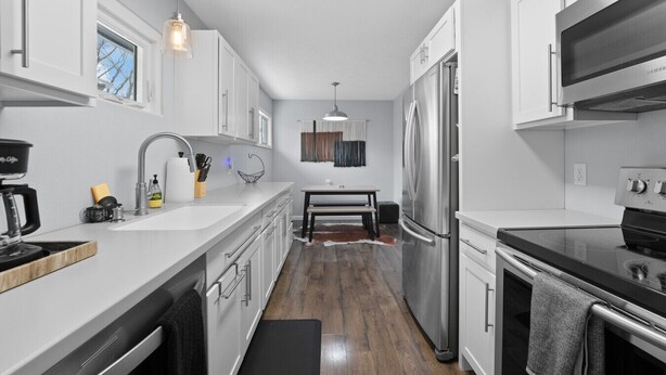 A modern kitchen with white cabinetry, stainless steel appliances, a coffee maker, and a dining area with a table and chairs.