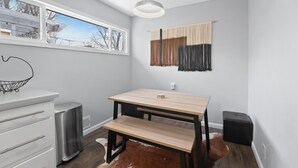 A modern kitchen with a wooden table, white cabinetry, a radiator, and a cowhide rug.
