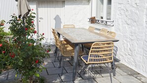 A patio with a wooden table and wicker chairs, surrounded by a white wall and a potted plant with red flowers. - The "Smoking Fox". Between the Meuse and Molignée rivers, relaxation and leisure! (Onhaye)