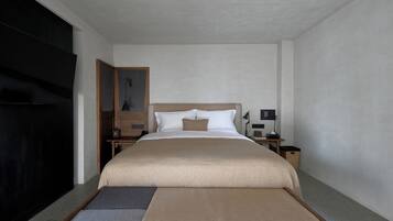 Una habitación de hotel con una cama grande, una mesita de noche de madera, un escritorio y una silla.