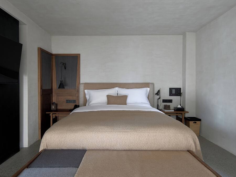 Una habitación de hotel con una cama grande, una mesita de noche de madera, un escritorio y una silla.